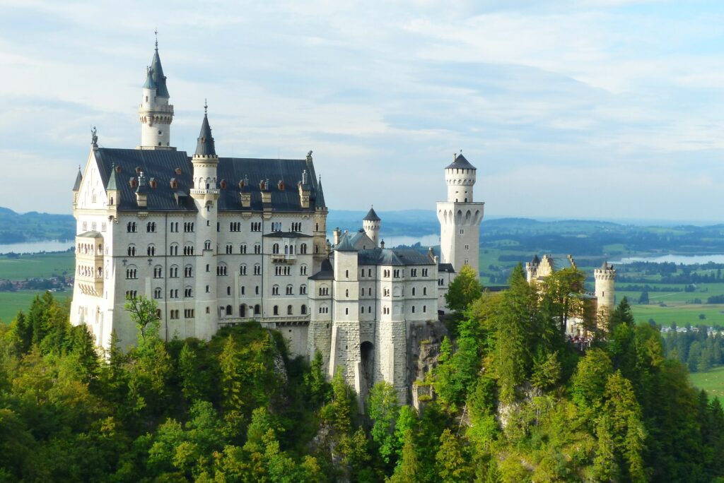 view of Neuschwanstein Castle on the top of the hill, surrounded by green forest lands