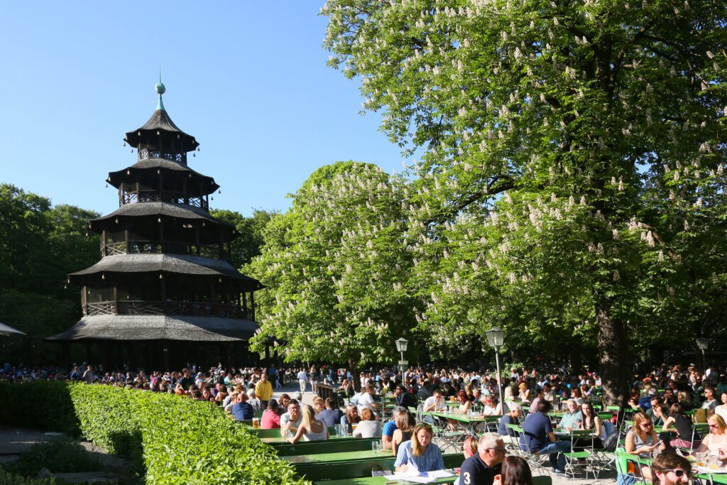 Beergarden visitors sit at long tables in front of the pagoda at Chinese Tower Beer Garden in the English Garden in Munich