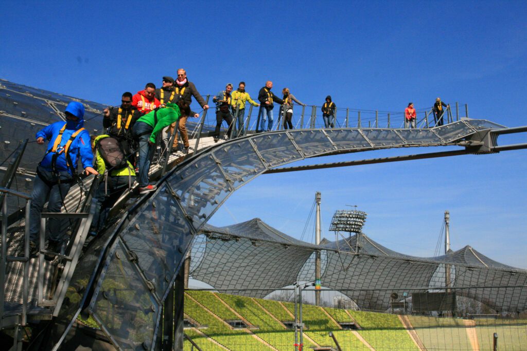 A group of people, with harnesses, climbing the roof of Olympic stadium.