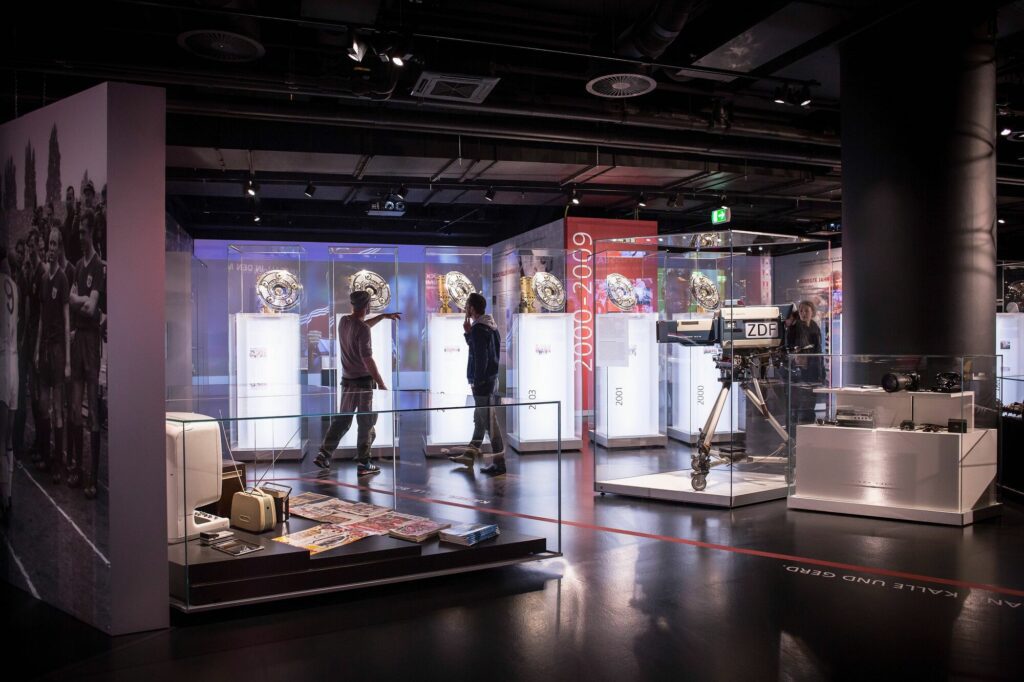 two men looking at trophies behind glass inside FC Bayern Munich Museum