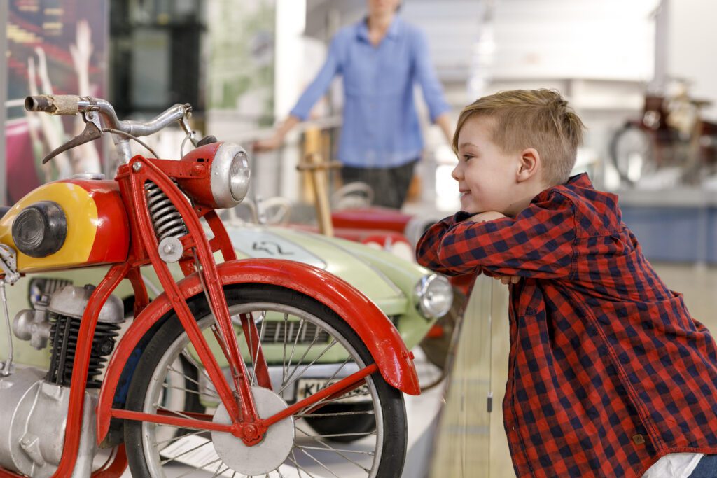 a boy is looking at a red motorbicycles, part of the exhibiton at transport museum munich